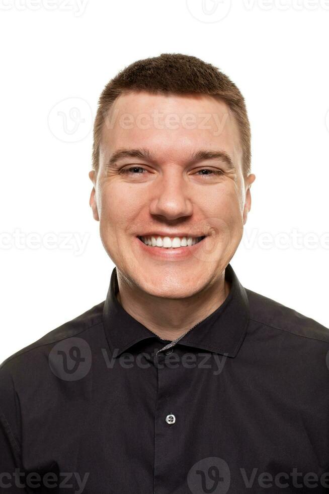 Handsome young man in a black shirt is making faces, while standing isolated on a white background photo