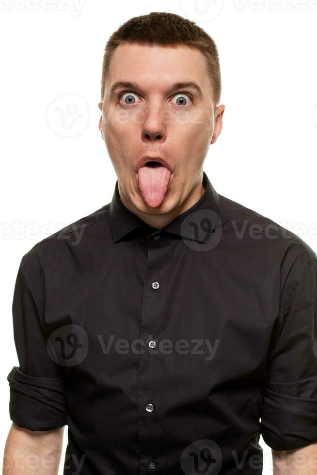 Handsome young man in a black shirt is making faces, while standing isolated on a white background photo