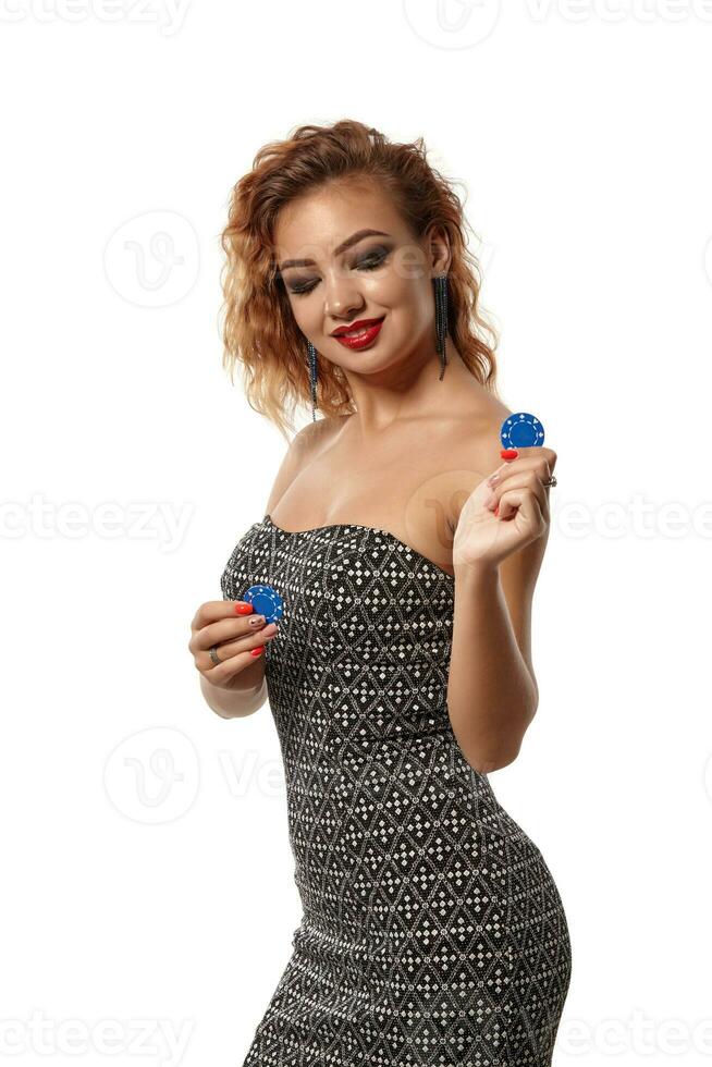 Ginger girl wearing gray dress is posing holding blue chips in her hands standing isolated on white background. Casino, poker. Close-up shot. photo