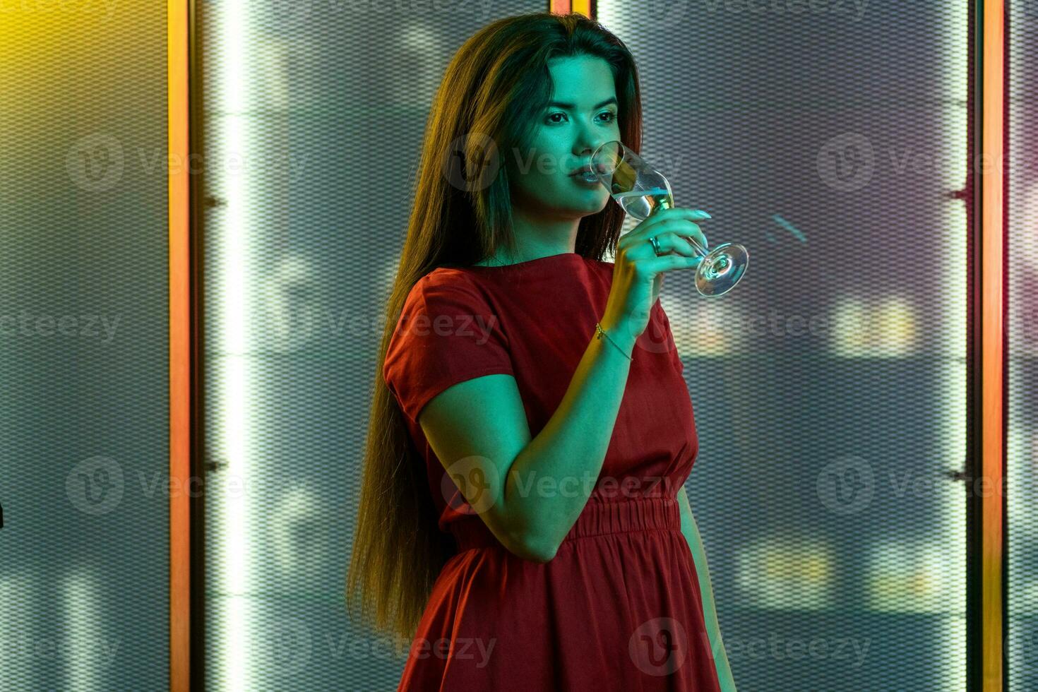 Stylish brunette enjoying sparkling wine in colored lighting of nightclub photo