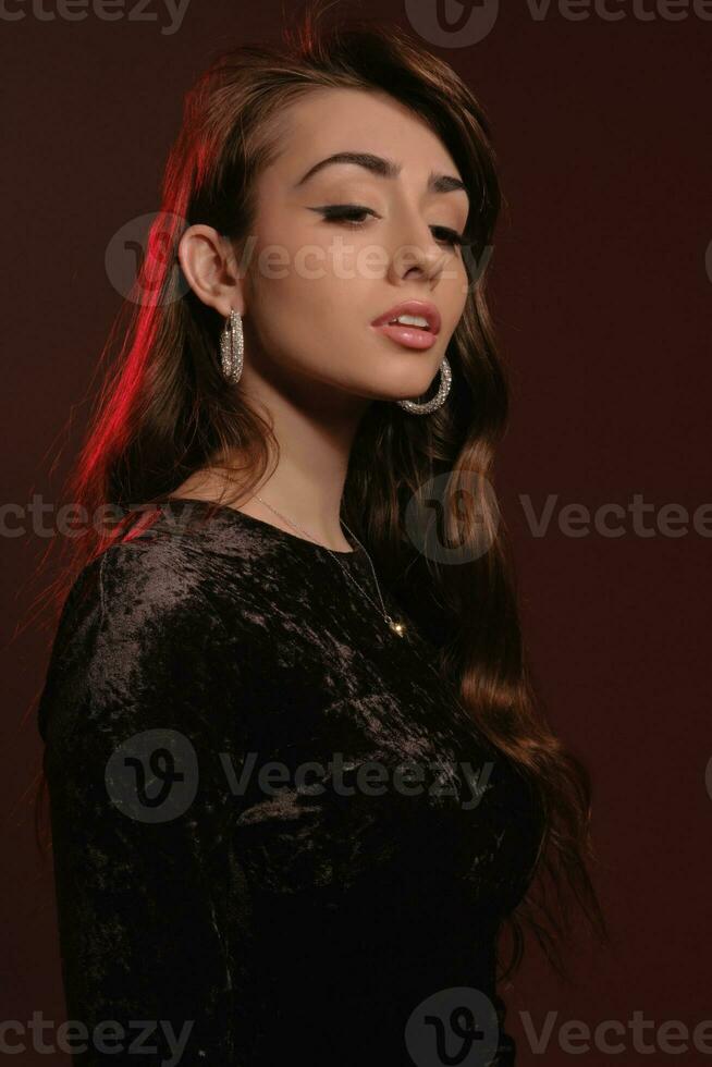 Attractive brunette lady in stylish jewelry and black velvet dress, posing against colorful background. Fashion and beauty. Close-up, copy space photo