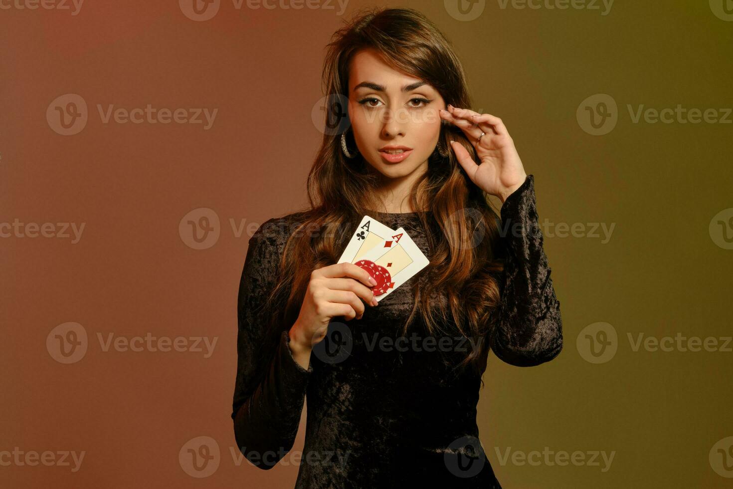 Brunette girl in black dress showing two red chips and aces, posing against colorful studio background. Gambling, poker, casino. Close-up. photo