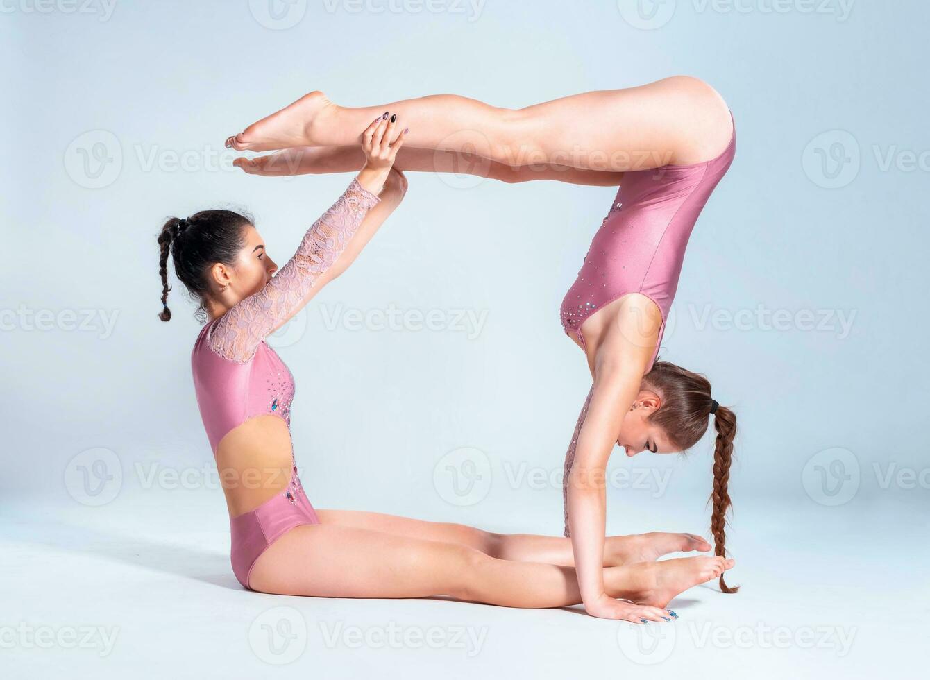 Two flexible girls gymnasts in pink leotards are doing exercises using support and posing isolated on white background. Close-up. photo