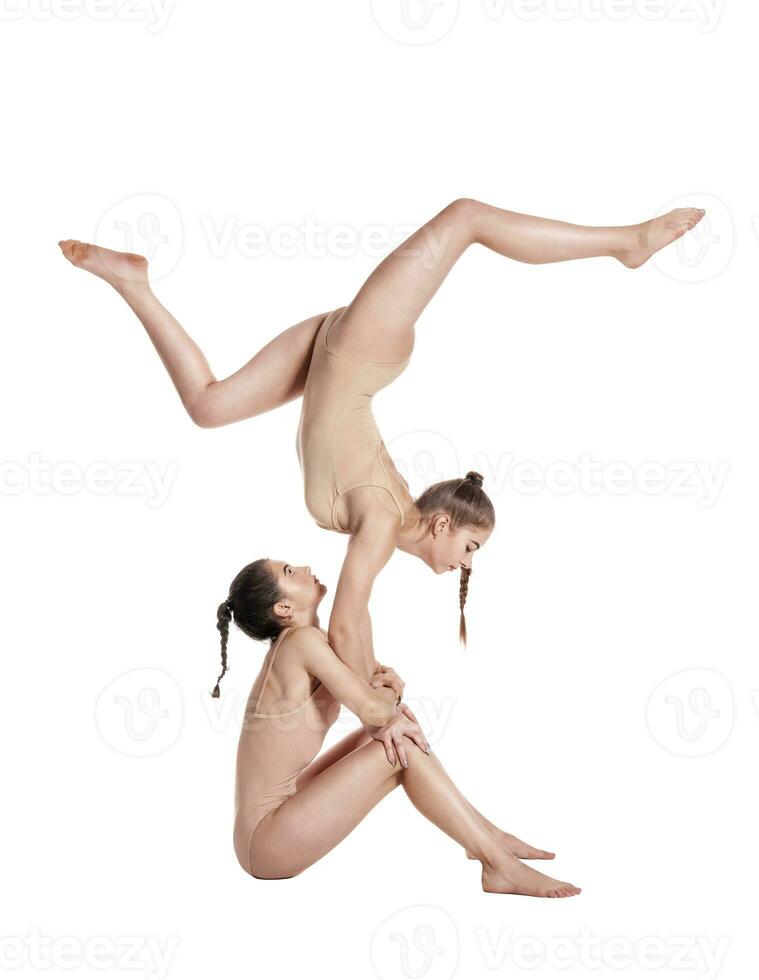 Two flexible girls gymnasts in beige leotards are performing exercises upside down using support and posing isolated on white background. Close-up. photo