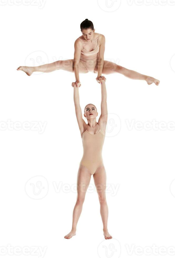 Two flexible girls gymnasts in beige leotards performing complex elements of gymnastics using support, posing isolated on white background. Close-up. photo