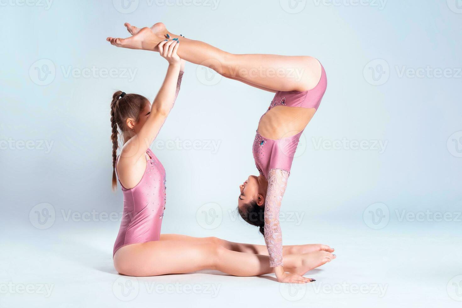 Two flexible girls gymnasts in pink leotards are doing exercises using support and posing isolated on white background. Close-up. photo