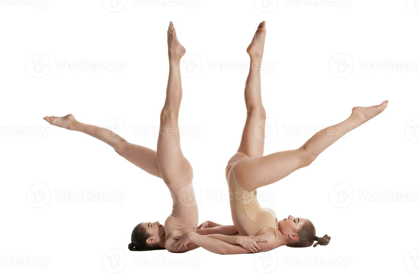 Two flexible girls gymnasts in beige leotards are performing exercises upside down using support and posing isolated on white background. Close-up. photo