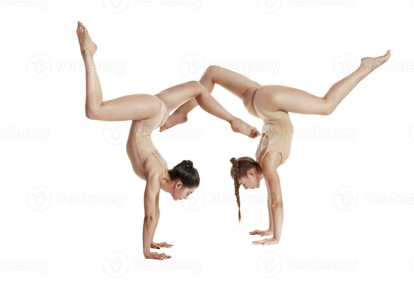 dos flexible muchachas gimnastas en beige leotardos ejecutando complejo elementos de gimnasia utilizando apoyo, posando aislado en blanco antecedentes. de cerca. foto