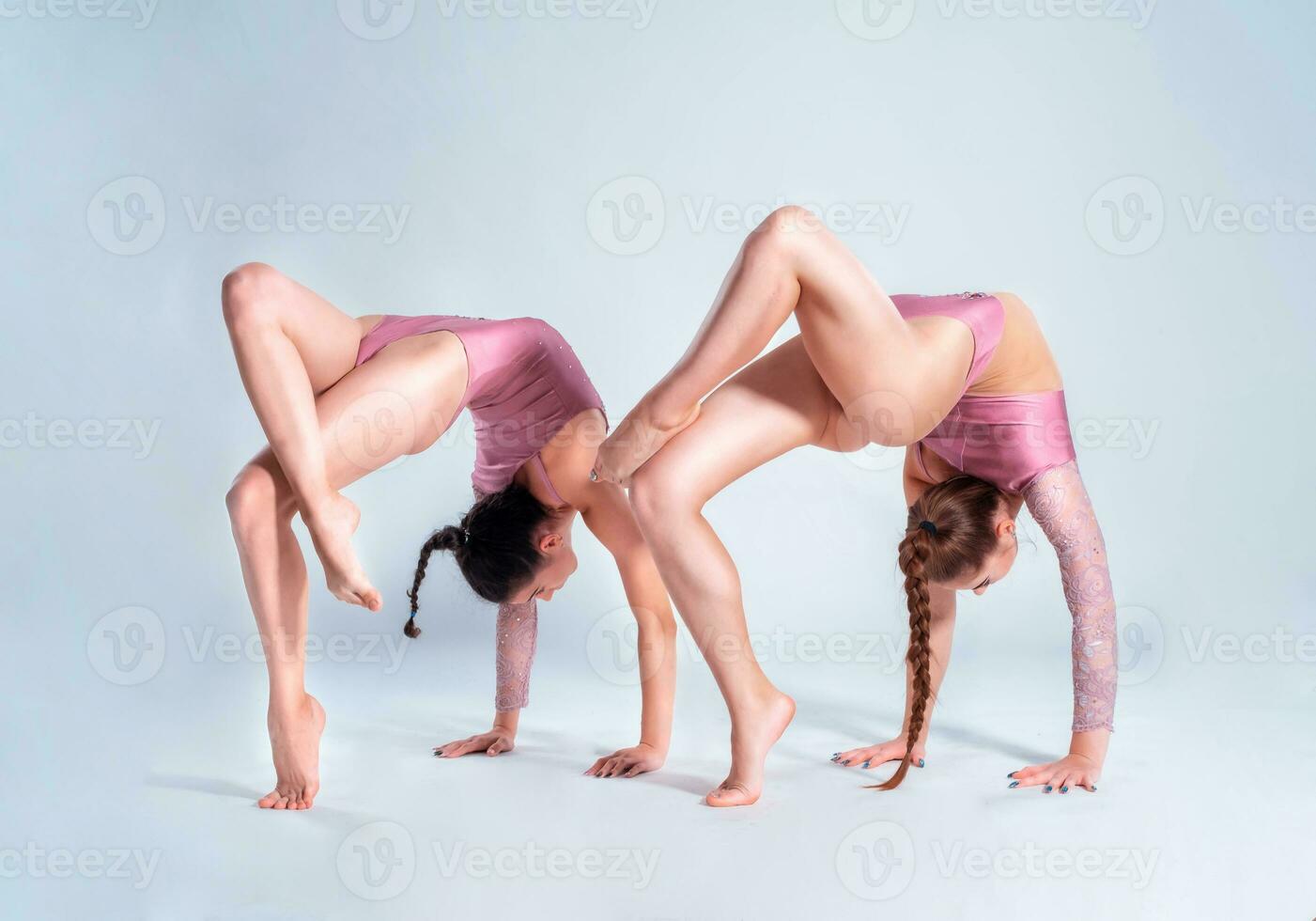 dos flexible muchachas gimnastas en beige leotardos ejecutando complejo elementos de gimnasia utilizando apoyo, posando aislado en blanco antecedentes. de cerca. foto