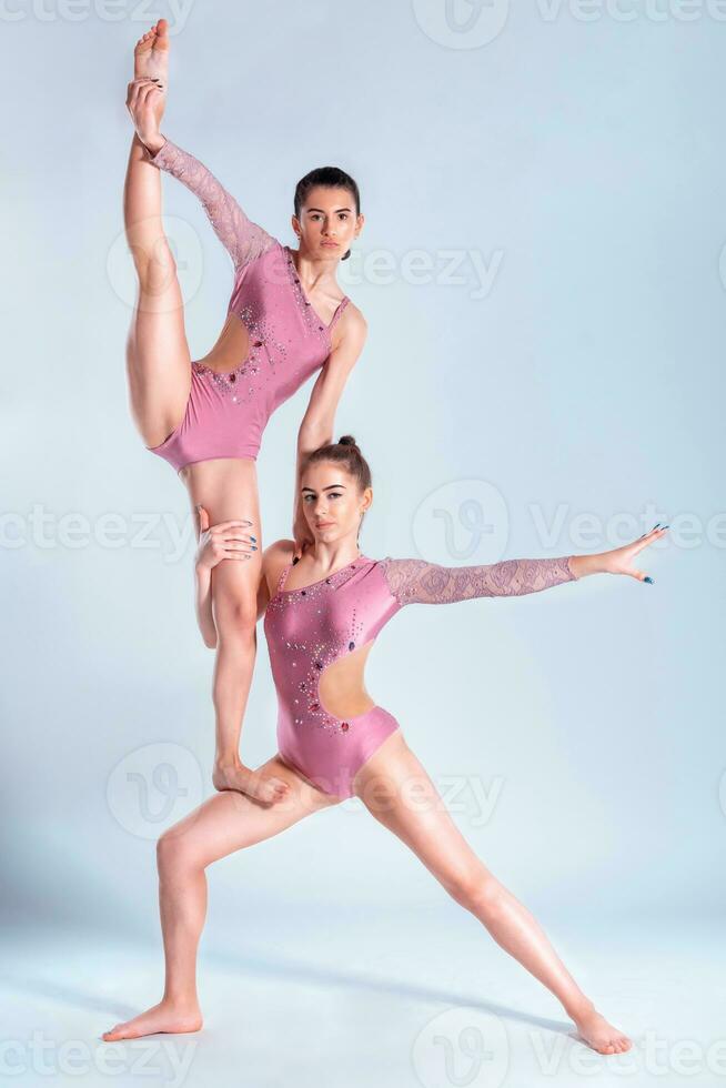 dos flexible muchachas gimnastas en beige leotardos ejecutando complejo elementos de gimnasia utilizando apoyo, posando aislado en blanco antecedentes. de cerca. foto