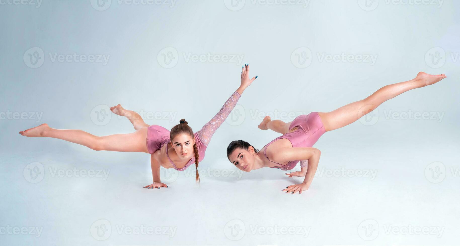 dos flexible muchachas gimnastas en beige leotardos ejecutando complejo elementos de gimnasia utilizando apoyo, posando aislado en blanco antecedentes. de cerca. foto