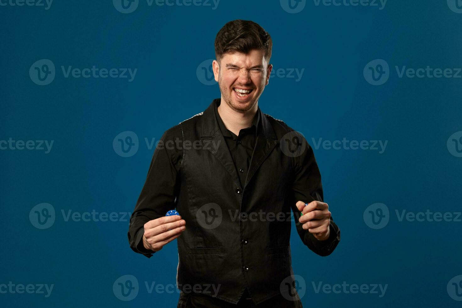 novato en póker, en negro chaleco y camisa. participación algunos de colores papas fritas. posando en contra azul antecedentes. juego, casino. de cerca. foto