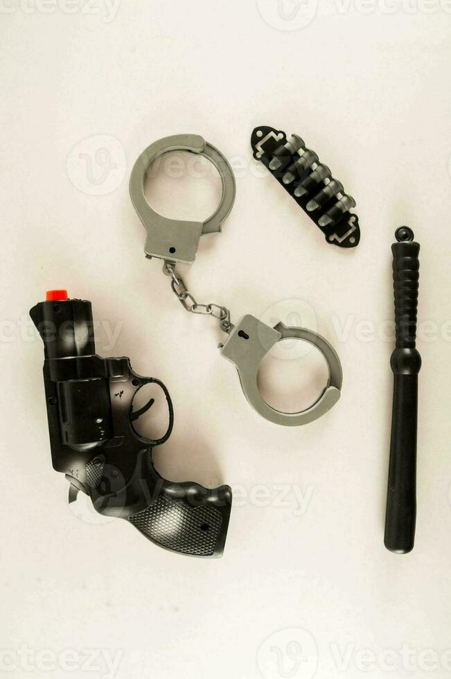 a toy gun, handcuffs, baton and knife on a white surface photo