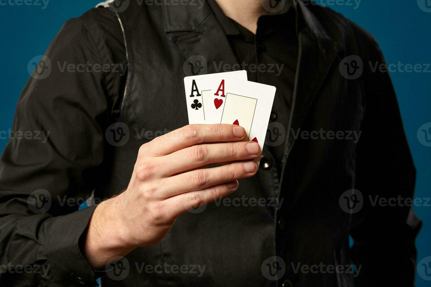 Newbie in poker, in black vest and shirt. Holding two playing cards while posing against blue studio background. Gambling, casino. Close-up. photo