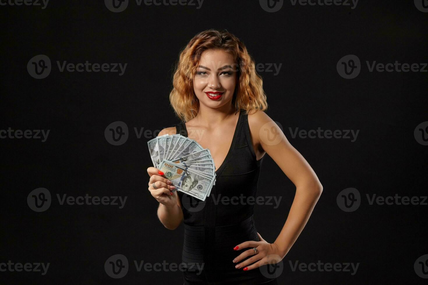 jengibre niña en oscuro vestir posando participación ventilador de cien dolares cuentas en su manos en pie en contra un negro estudio antecedentes. casino, póker. de cerca. foto