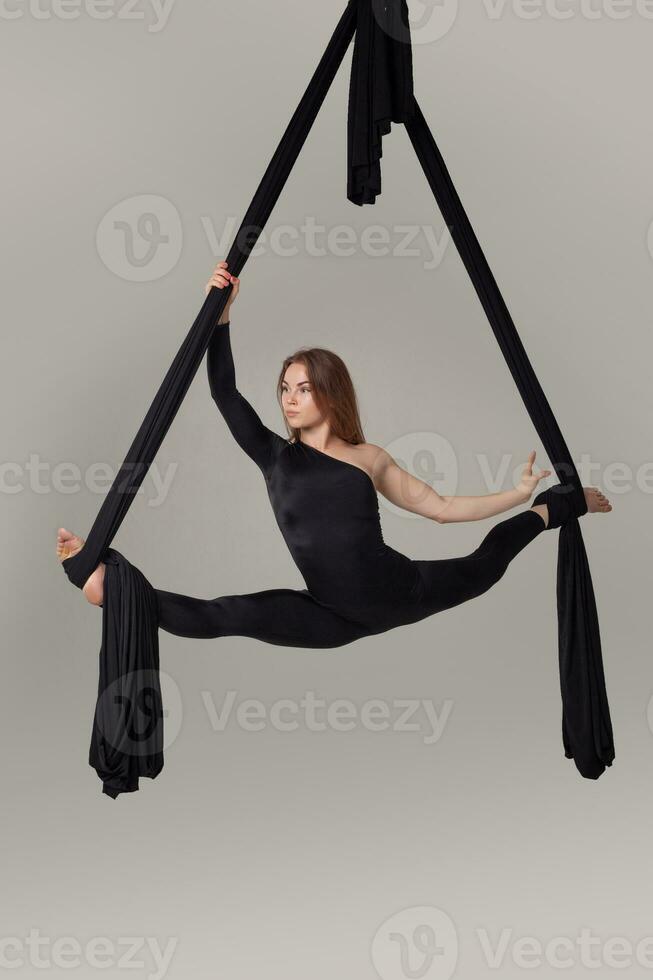 hermosa niña en un negro deporte traje es ejecutando un acrobático elementos en un estudio. foto