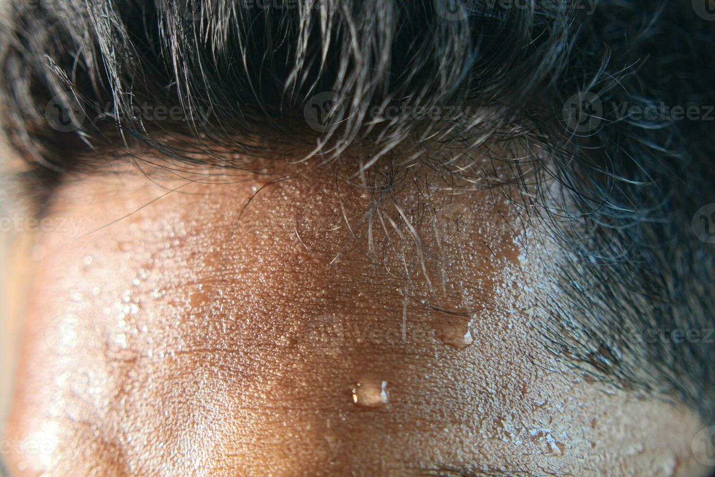 closeup of sweat on forehead against dark background , photo