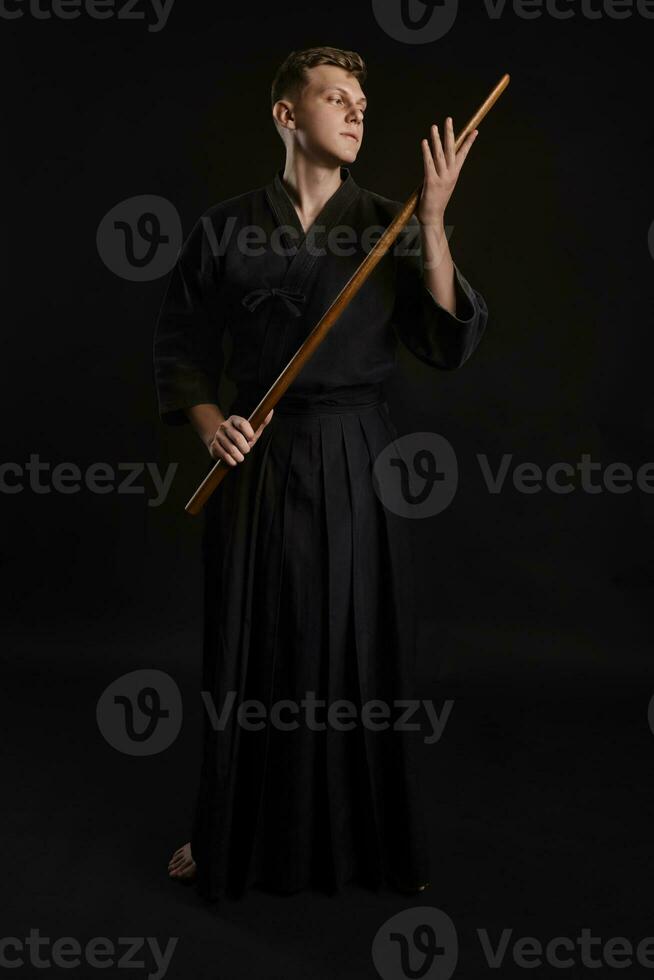 Kendo guru wearing in a traditional japanese kimono is practicing martial art with the shinai bamboo sword against a black studio background. photo