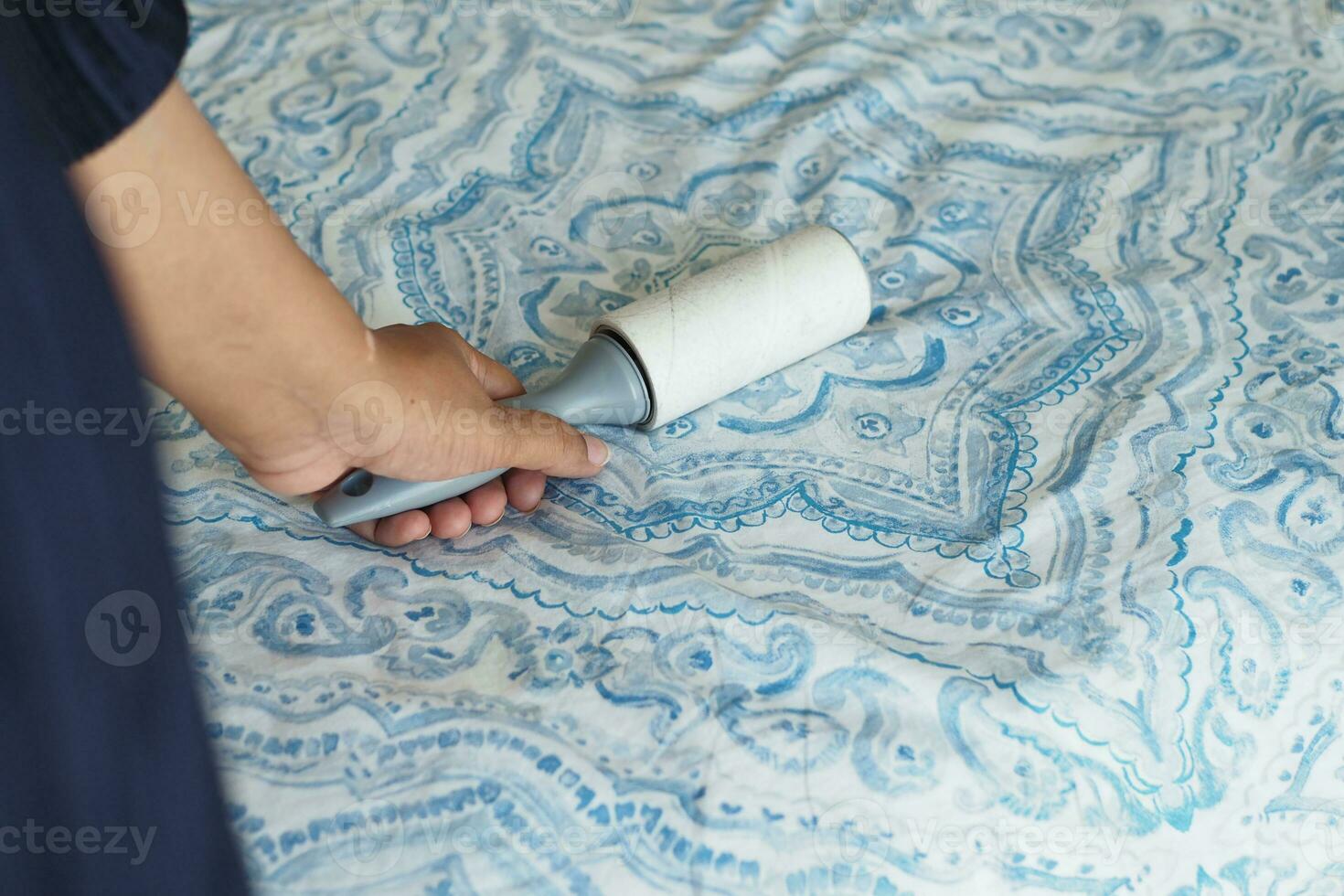 using an adhesive roller to remove lint and fluff from a bed . photo