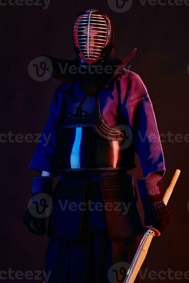Close up shot, Kendo fighter wearing in an armor, traditional kimono, helmet practicing martial art with shinai bamboo sword, black background. photo
