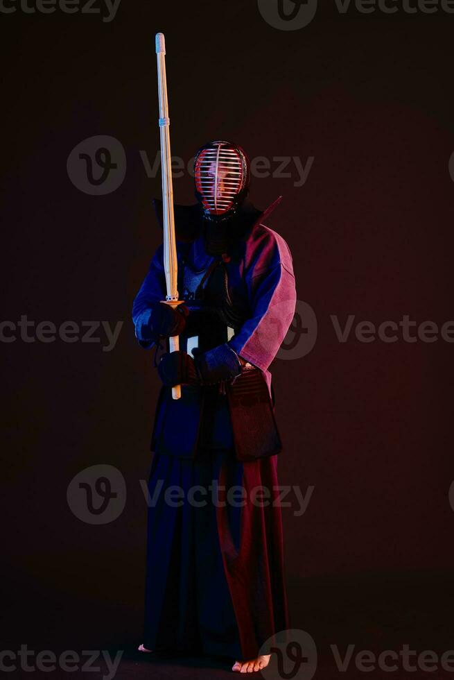 cerca arriba disparo, kendo combatiente vistiendo en un armadura, tradicional kimono, casco practicando marcial Arte con shinai bambú espada, negro antecedentes. foto