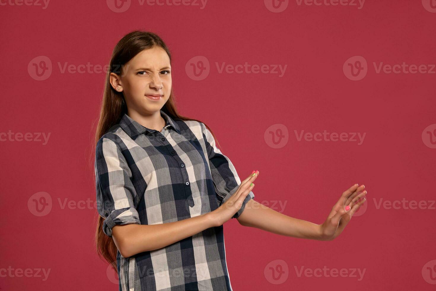 Beautiful teenage girl in a casual checkered shirt is posing against a pink studio background. photo