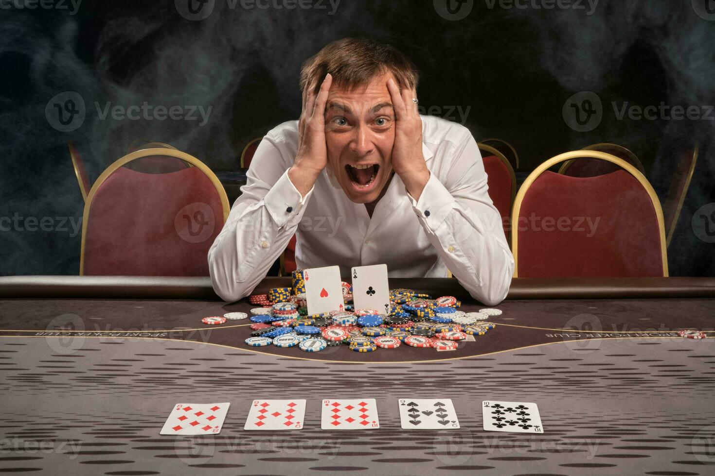 Handsome emotional man is playing poker sitting at the table in casino. photo