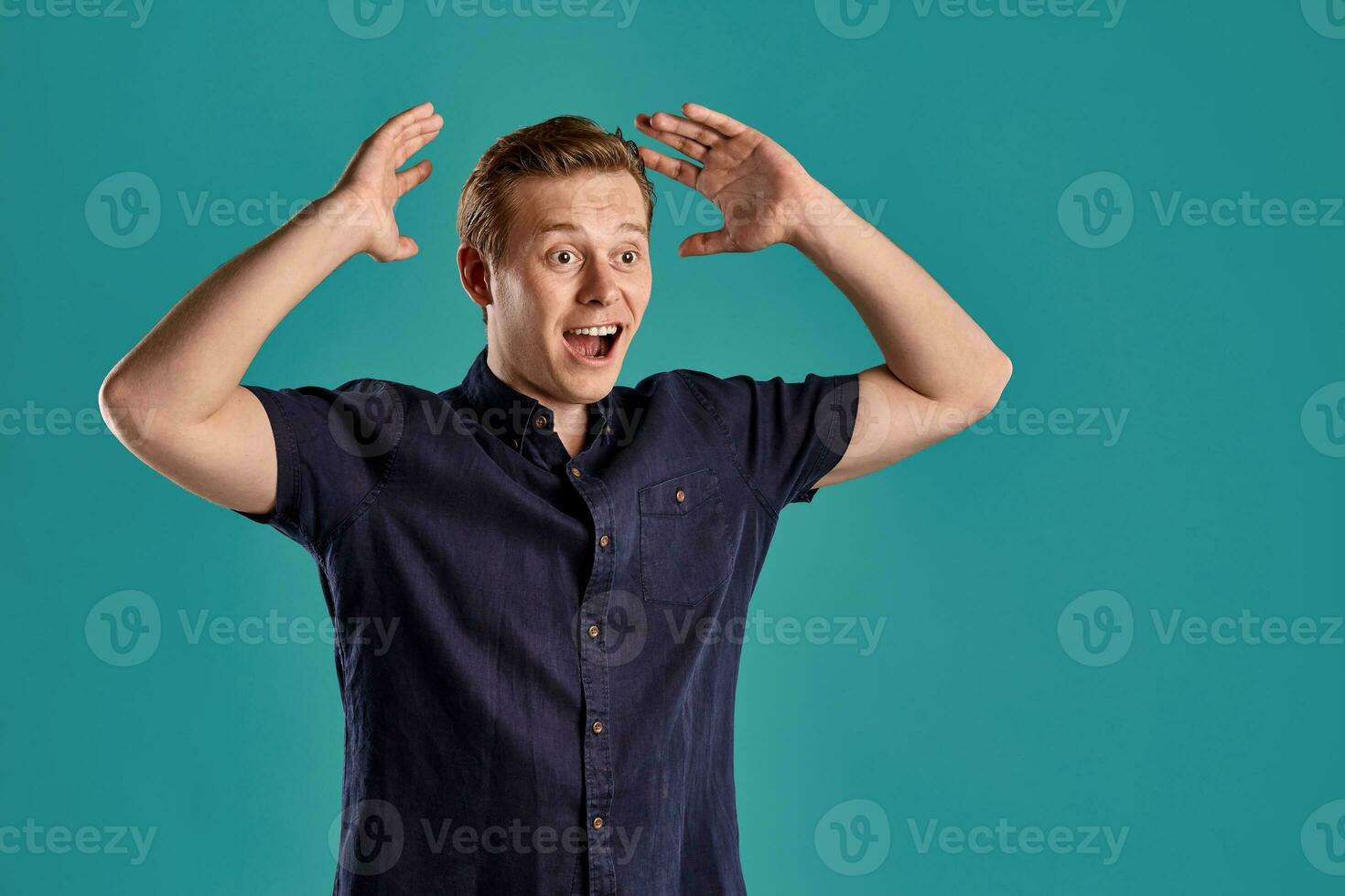 Close-up portrait of a ginger guy in navy t-shirt posing on blue background. Sincere emotions. photo