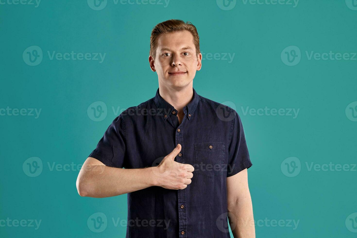 Close-up portrait of a ginger guy in navy t-shirt posing on blue background. Sincere emotions. photo