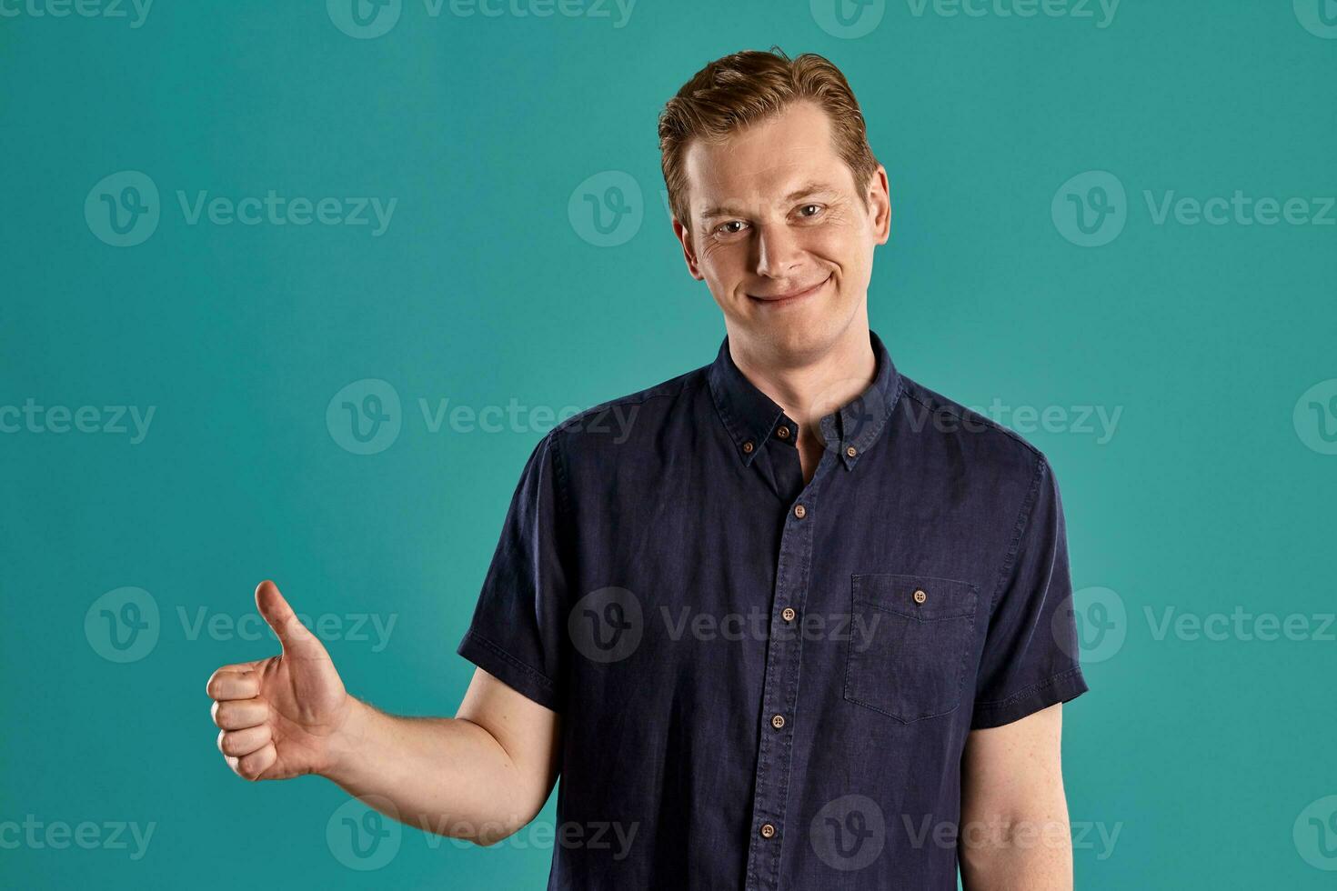 Close-up portrait of a ginger guy in navy t-shirt posing on blue background. Sincere emotions. photo