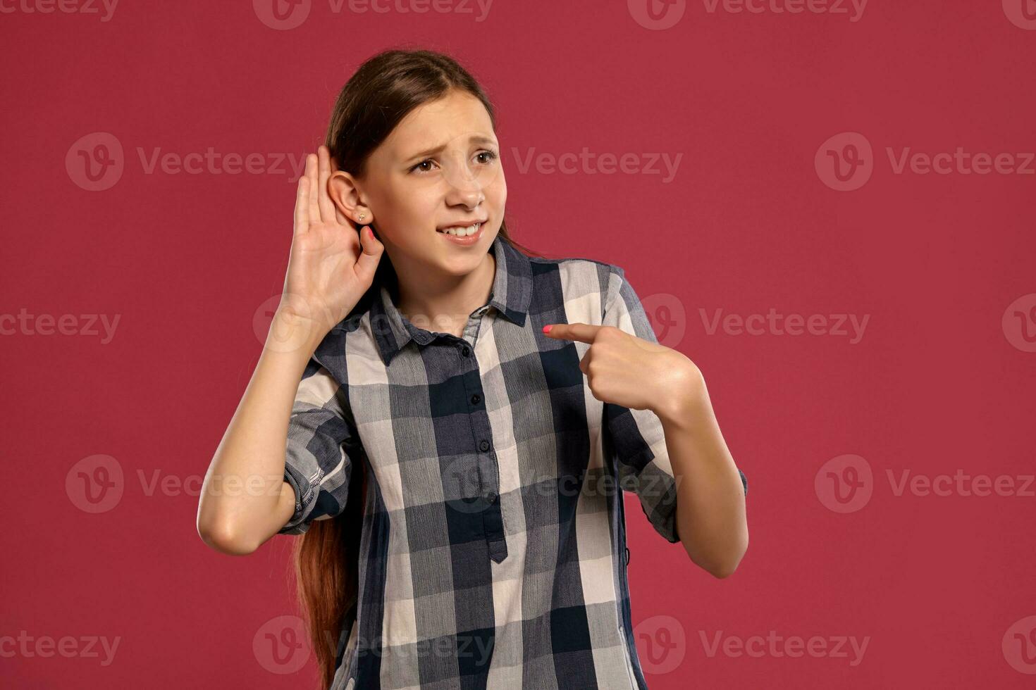 Beautiful teenage girl in a casual checkered shirt is posing against a pink studio background. photo