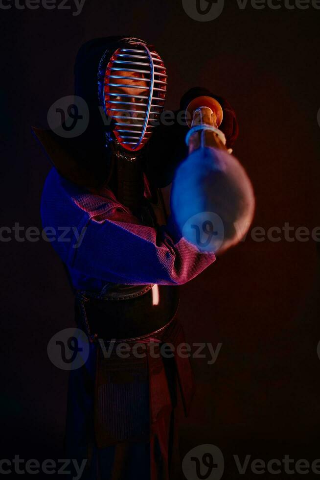 Close up shot, Kendo fighter wearing in an armor, traditional kimono, helmet practicing martial art with shinai bamboo sword, black background. photo