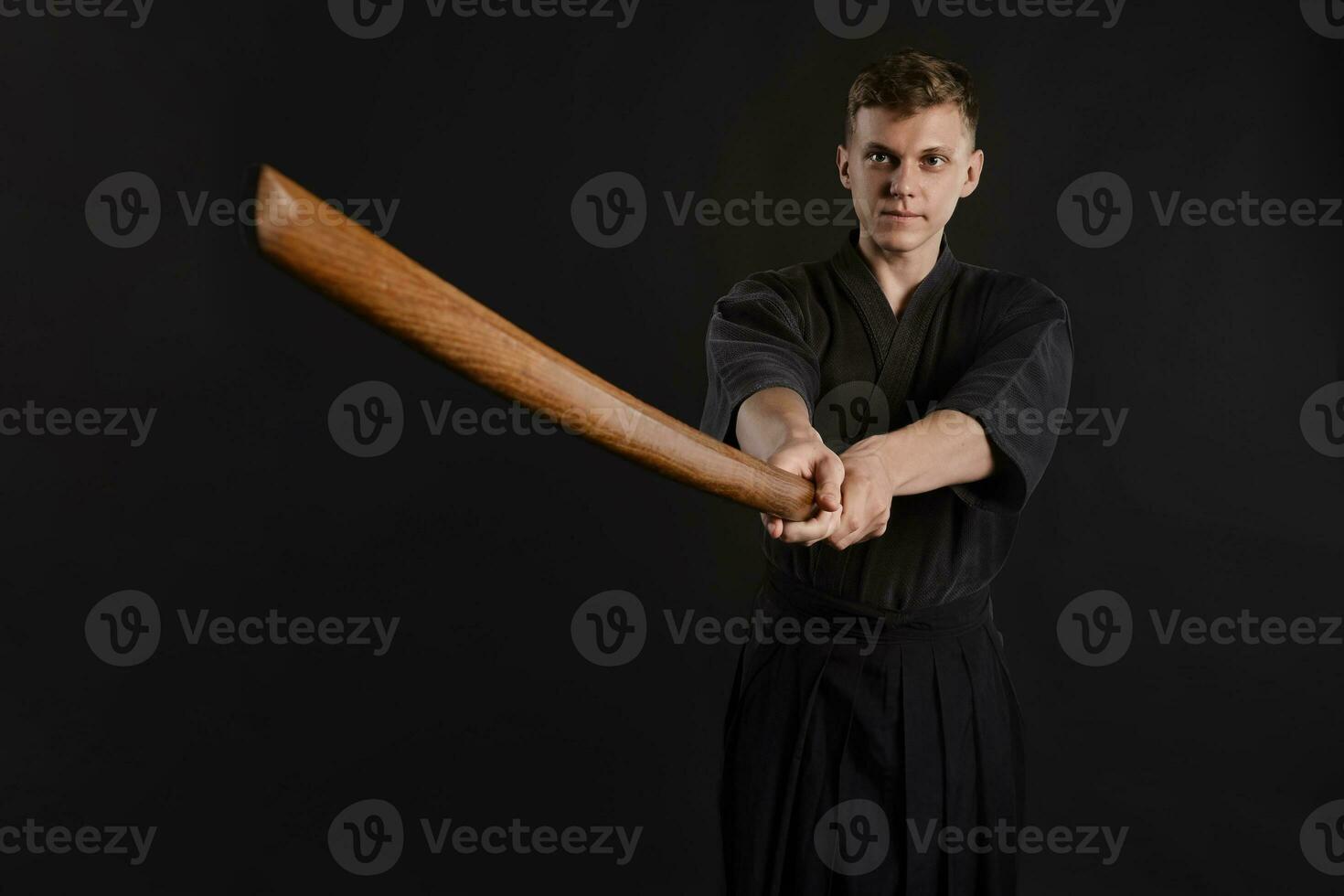 Kendo guru wearing in a traditional japanese kimono is practicing martial art with the shinai bamboo sword against a black studio background. photo