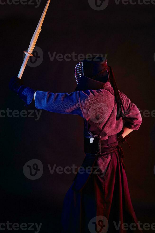 cerca arriba disparo, kendo combatiente vistiendo en un armadura, tradicional kimono, casco practicando marcial Arte con shinai bambú espada, negro antecedentes. foto