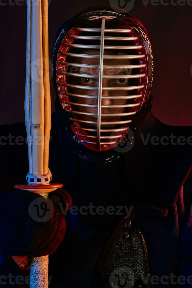 Close up shot, Kendo fighter wearing in an armor, traditional kimono, helmet practicing martial art with shinai bamboo sword, black background. photo