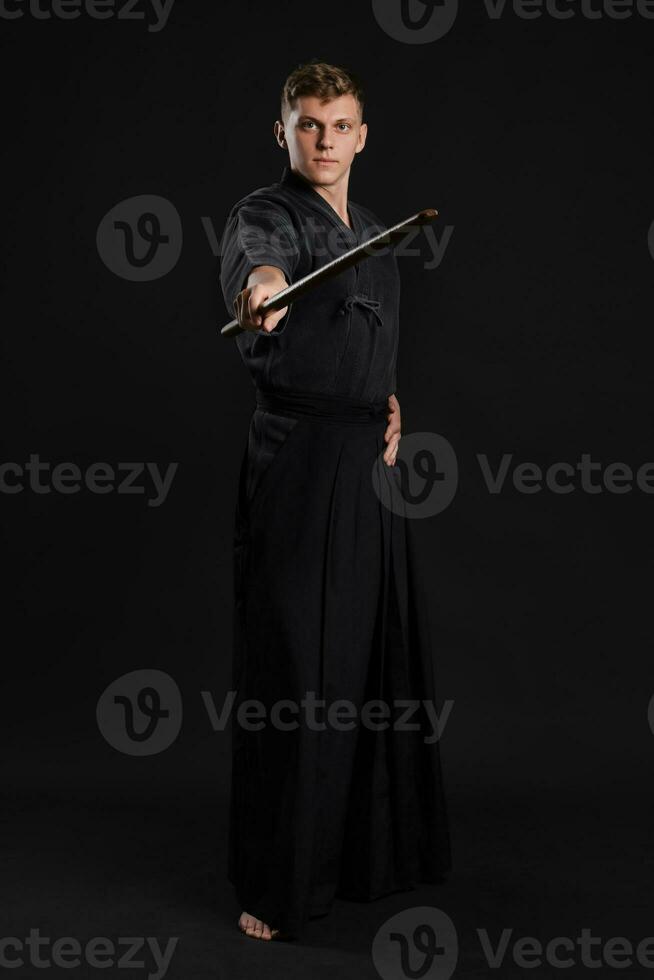 Kendo guru wearing in a traditional japanese kimono is practicing martial art with the shinai bamboo sword against a black studio background. photo