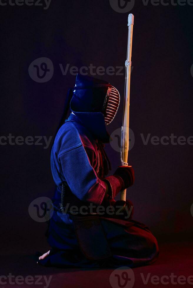 cerca arriba disparo, kendo combatiente vistiendo en un armadura, tradicional kimono, casco practicando marcial Arte con shinai bambú espada, negro antecedentes. foto