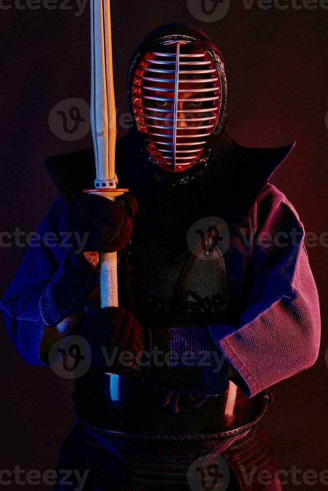 cerca arriba disparo, kendo combatiente vistiendo en un armadura, tradicional kimono, casco practicando marcial Arte con shinai bambú espada, negro antecedentes. foto