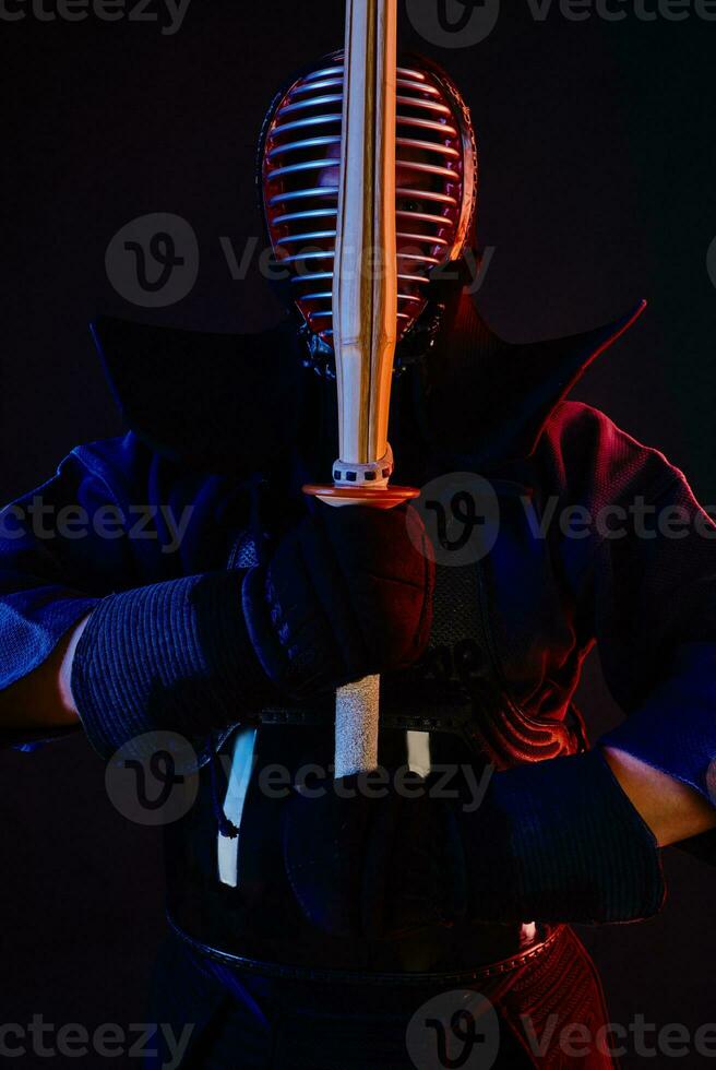 Close up shot, Kendo fighter wearing in an armor, traditional kimono, helmet practicing martial art with shinai bamboo sword, black background. photo