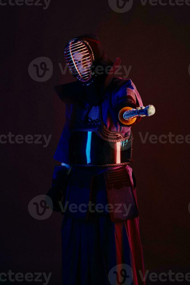 Close up shot, Kendo fighter wearing in an armor, traditional kimono, helmet practicing martial art with shinai bamboo sword, black background. photo