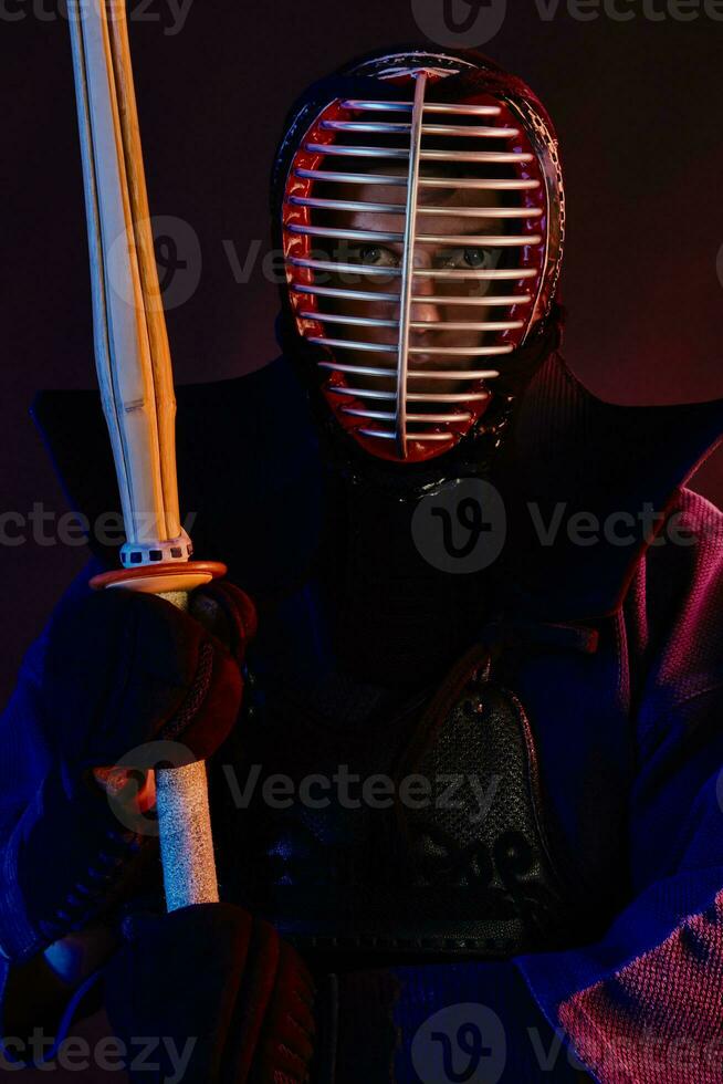 Close up shot, Kendo fighter wearing in an armor, traditional kimono, helmet practicing martial art with shinai bamboo sword, black background. photo