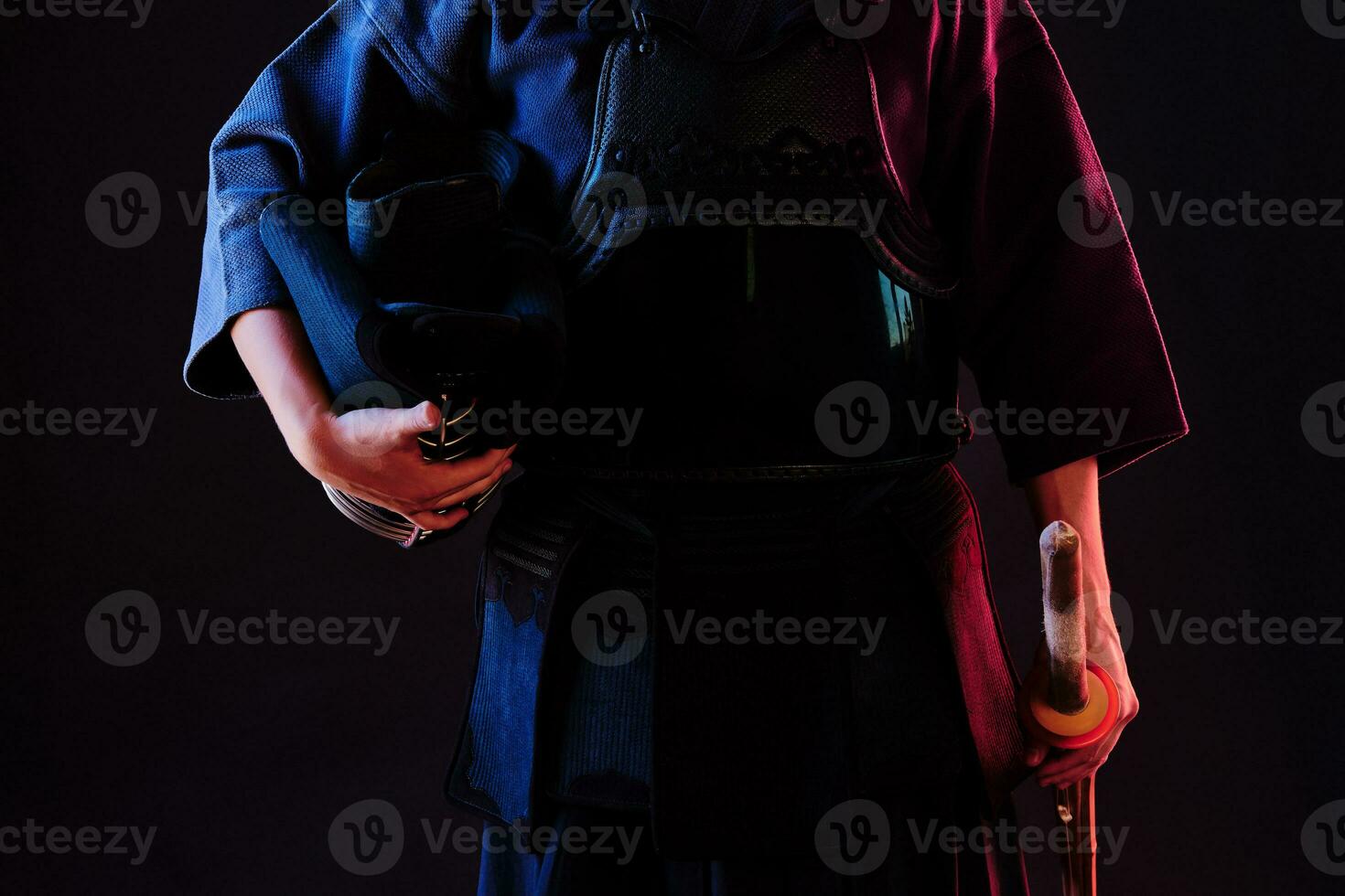 Kendo fighter wearing in an armor, traditional kimono is holding his helmet and shinai bamboo sword while posing on a black background. Close up. photo