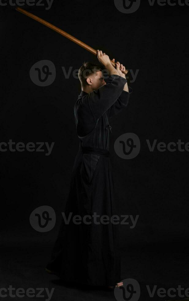 kendo gurú vistiendo en un tradicional japonés kimono es practicando marcial Arte con el shinai bambú espada en contra un negro estudio antecedentes. foto