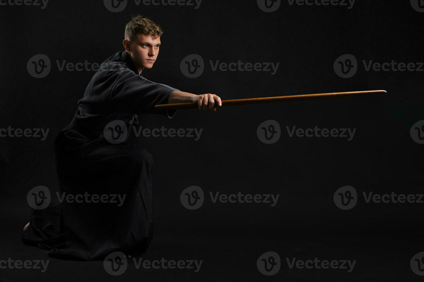 Kendo guru wearing in a traditional japanese kimono is practicing martial art with the shinai bamboo sword against a black studio background. photo