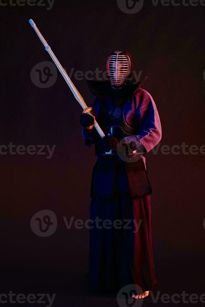 Close up shot, Kendo fighter wearing in an armor, traditional kimono, helmet practicing martial art with shinai bamboo sword, black background. photo