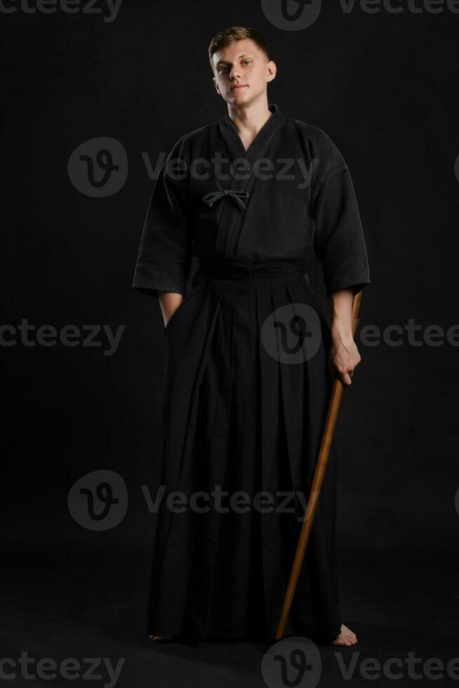 Kendo guru wearing in a traditional japanese kimono is practicing martial art with the shinai bamboo sword against a black studio background. photo