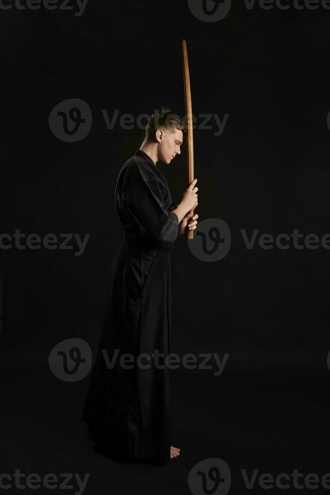 kendo gurú vistiendo en un tradicional japonés kimono es practicando marcial Arte con el shinai bambú espada en contra un negro estudio antecedentes. foto