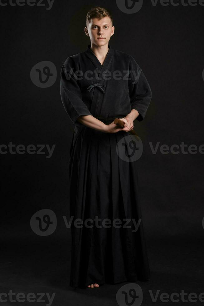 Kendo guru wearing in a traditional japanese kimono is practicing martial art with the shinai bamboo sword against a black studio background. photo