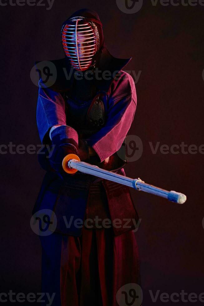 Close up shot, Kendo fighter wearing in an armor, traditional kimono, helmet practicing martial art with shinai bamboo sword, black background. photo