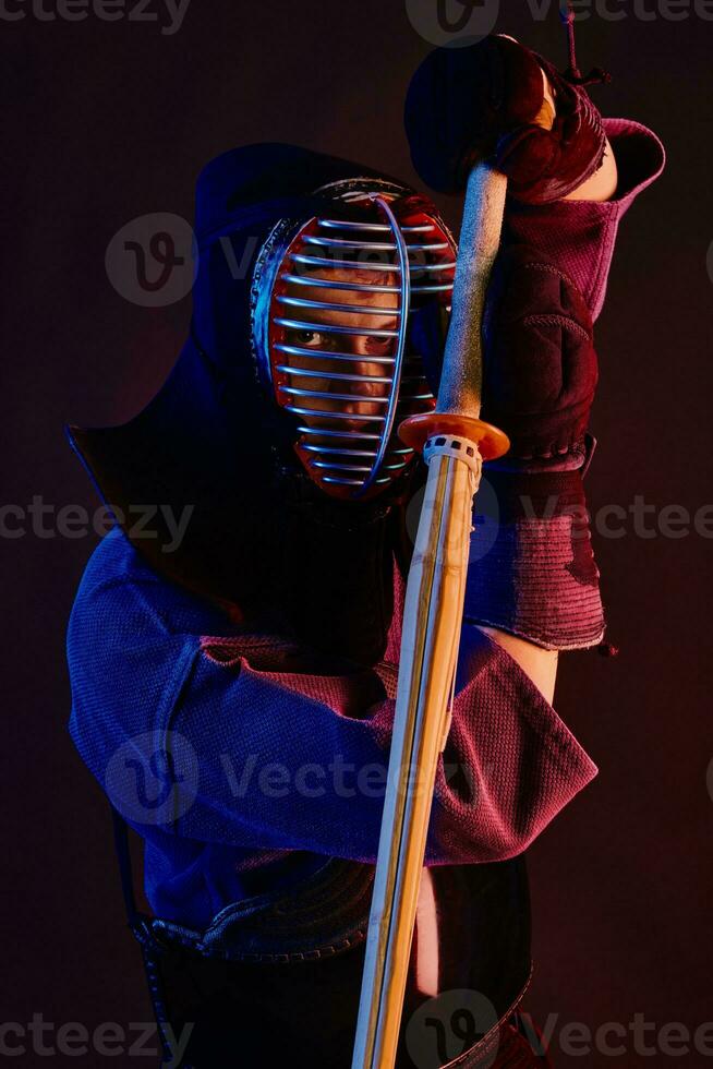 cerca arriba disparo, kendo combatiente vistiendo en un armadura, tradicional kimono, casco practicando marcial Arte con shinai bambú espada, negro antecedentes. foto